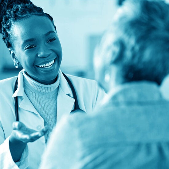 African American healthcare professional wearing a white lab coat and a stethoscope, smiling as she converses with an older patient