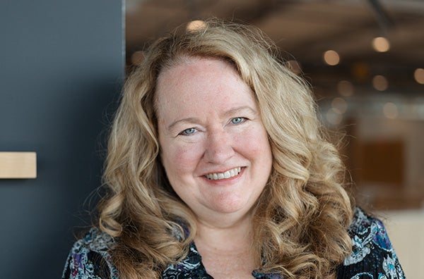 Theresa Eagleson with long blonde hair and wearing a blue top and necklace, smiling into the camera